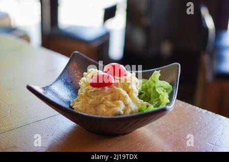 mashed potato salad with sliced cherry tomato and lettuce in black bowl on wooden table Stock Photo