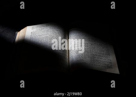 Old Bible, open book on black background, grazing light Stock Photo