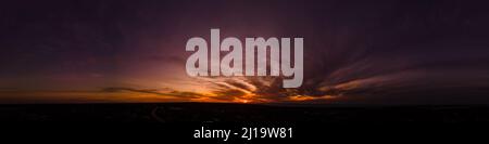 Dark wispy clouds in a deep purple sky at the end of a glowing orange sunset aerial panoramic Stock Photo