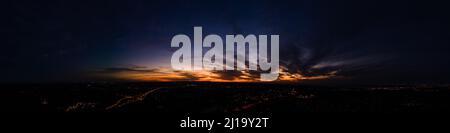 Dark wispy clouds in a deep blue sky in the afterglow of an golden sunset above the street lights aerial panoramic Stock Photo