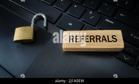 Referrals text on wooden blocks with pad lock and laptop background. Online business concept Stock Photo