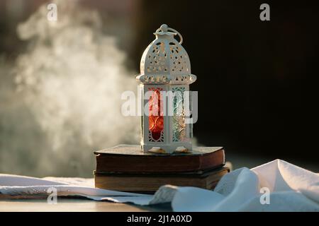 Ramadan Kareem background. Ornamental Arabic lantern glowing at night and the holy book of Quran. Stock Photo