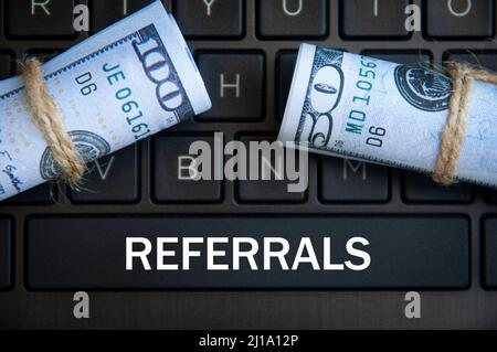 Referrals text on laptop space bar with bank notes and laptop background. Online business concept Stock Photo