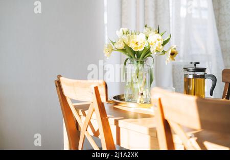 Beautiful bouquet of yellow tulips in vase on dinner table in white kitchen light interior at home Stock Photo