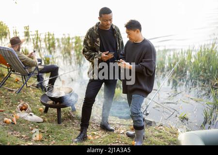 Men using smartphones during resting on pond coast Stock Photo