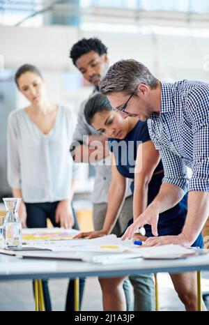 Leading the way with creative collaborations. Male and female managers planning at a table with younger staff members looking on. Stock Photo