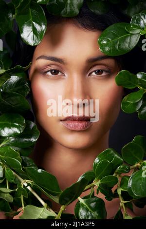 Wrapped in natures beauty. Studio shot of an attractive young ethnic woman surrounded by leaves. Stock Photo