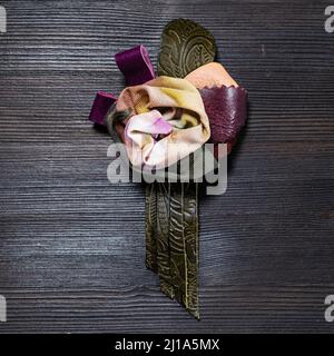 top view of handcrafted leather and silk brooch stylized as rose flower on dark wooden board Stock Photo