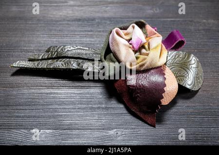 handcrafted leather and silk brooch stylized as rose flower close up on dark wooden board Stock Photo