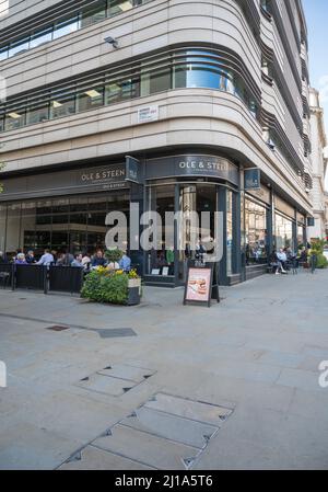 People socialise and enjoy food and drink seated at pavement tables outside Ole & Steen bakery and coffee shop. Haymarket, London, England, UK Stock Photo