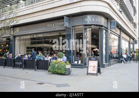 People socialise and enjoy food and drink seated at pavement tables outside Ole & Steen bakery and coffee shop. Haymarket, London, England, UK Stock Photo