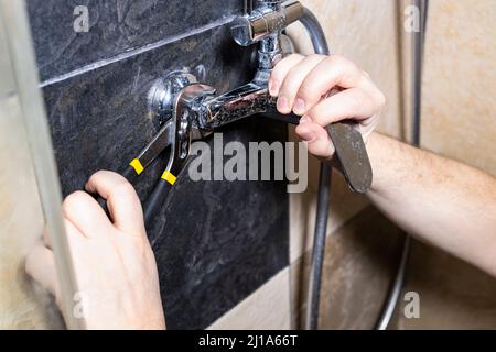 plumber installs shower faucet on tiled wall at home Stock Photo