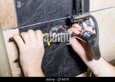 plumber unscrews shower faucet on tiled wall at home Stock Photo