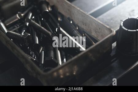 Selective focus on threaded tap, metal drill bit, and nut in old and dirty plastic toolbox. Old steel tool in box. Carbide tip metal cutter. Metalwork Stock Photo