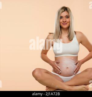 pregnant woman in lotus position applying cosmetic cream on her belly to avoid stretch marks Stock Photo