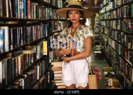 Beautiful girl wearing stylish outfit looking for interesting book in the vintage bookstore Stock Photo