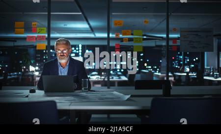 Successful Senior Businessman Working on Laptop Computer in Big City Office Late in the Evening. Investment Analyst Checking Financial Management Repo Stock Photo