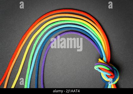 Seven dyed cotton cords shaped into a rainbow symbol and knotted together on a black background. Hope and solidarity concept. Stock Photo