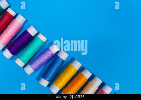 A set of multi-colored threads for sewing with an empty space for text on a blue background, top view. Tailoring and needlework equipment, tailor Stock Photo