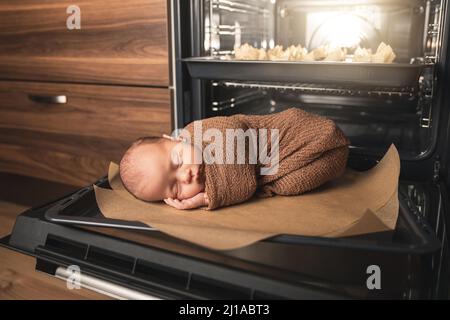 Newborn baby is lying on the oven tray with a muffins Stock Photo