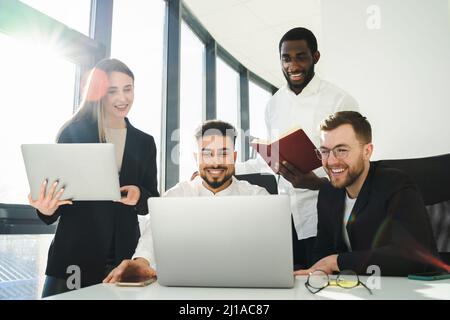 Group of multiracial office workers laughing while looking at laptop.  Employees of the company are working on a new project Stock Photo