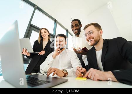 Group of office workers laughing while looking at laptop during meeting in office Stock Photo