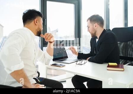 Two businessmen analyze the growth of the company sitting at the laptop in the office Stock Photo