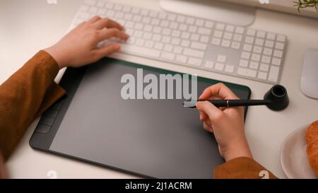 Close-up image, Female freelance graphic designer or photo editor using on graphic tablet and working on computer at her office desk. Stock Photo
