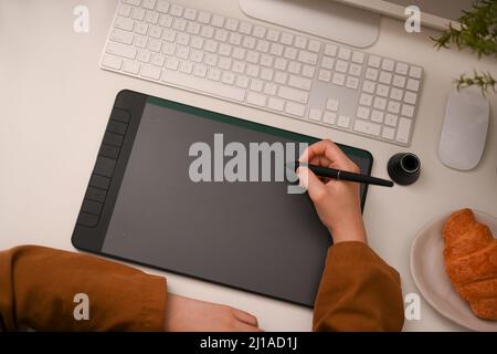 Top view, cropped image, Female graphic designer, artist or architect using graphic tablet and looking at computer screen in her office desk. Stock Photo