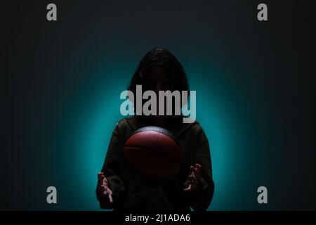 Teenage girl with basketball. Silhouette studio portrait with neon blue colored background. Stock Photo