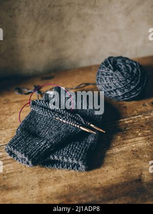 Hand knitted sock with needles and grey yarn ball on dark wooden background. Concept for handmade and hugge slow life. Stock Photo