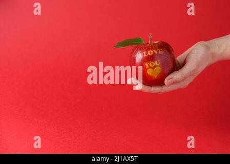 Red apple with text I Love You on red background in hand Stock Photo