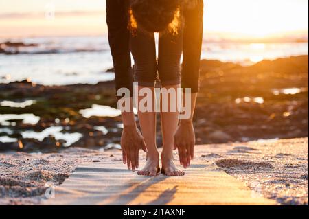 My hamstrings needed this stretch. Cropped shot of an unrecognizable woman doing yoga alone on the beach at sunset. Stock Photo