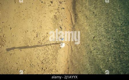 Zero pollution is the only solution. High angle shot of a woman walking along the coast of an Indonesian island with a rake. Stock Photo
