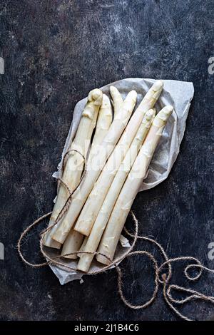 Raw white asparagus on a dark textured background. Raw food concept. Stock Photo