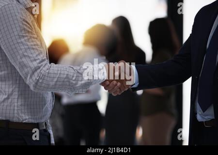 Welcome to our team. Shot of two silhouetted businesspeople shaking hands in front of a window in the office. Stock Photo