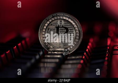 Bitcoin BTC cryptocurrency physical coin placed on the computer keyboard and lit with red light. Stock Photo