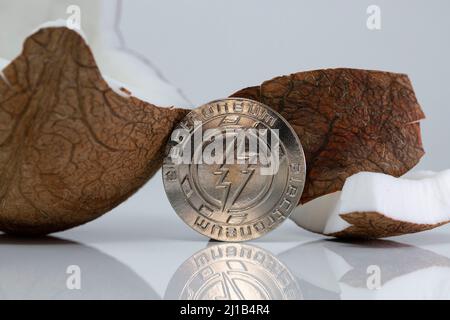 Electroneum ETN cryptocurrency physical coin placed next to broken coconut on the white reflective table. Macro Shot. Stock Photo