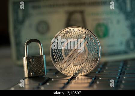 Stellar Lumens XLM cryptocurrency physical coin placed on laptop keyboard and dollar in the background Stock Photo