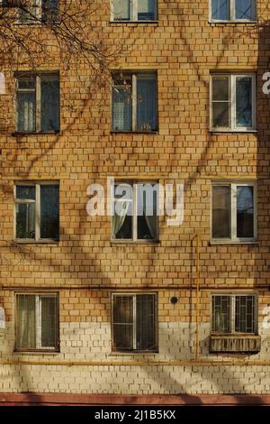 Russian panel house and windows of different apartments. Shadow from trees on house, winter landscape. Gas yellow pipe Stock Photo