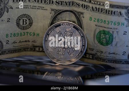 Cardano ADA cryptocurrency physical coin placed on computer keyboard with one dollar bill in the background Stock Photo
