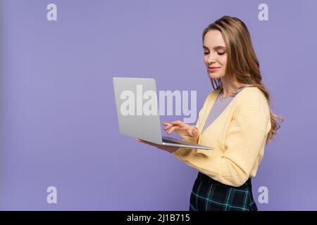 cheerful student using laptop isolated on purple Stock Photo
