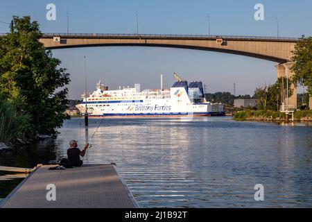 FISHERMAN IN FRONT OF THE BRITTANY FERRIES BOAT BENEATH THE CALIX VIADUCT ABOVE THE CANAL RUNNING FROM CAEN TO THE SEA, ORNE RIVER, CAEN, CALVADOS, NORMANDY, FRANCE Stock Photo