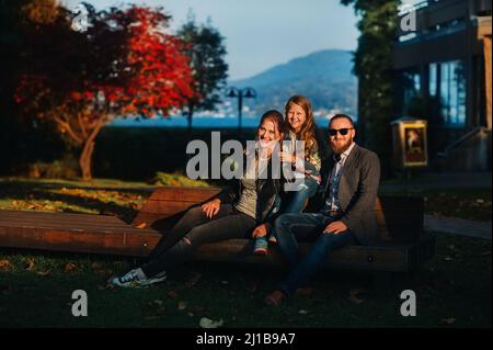 A happy family of three sits on a bench at a Sunny autumn sunset in Austria's Old town.A family poses in a small Austrian town against the backdrop of Stock Photo