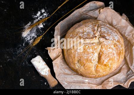 Fresh homemade crisp bread on Kraft paper with rye sticks and flour and over black table. Healthy baked bread on black wooden background. Stock Photo