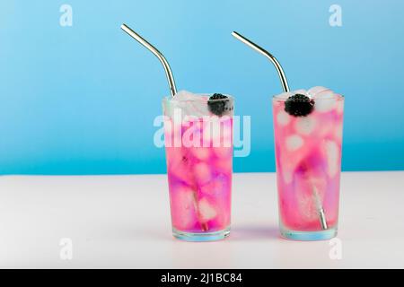 Summer refreshing pink cocktail with ice cube, metal straw and blackberry on blue background. Stock Photo