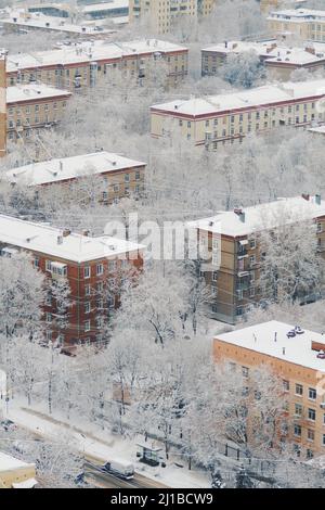 Snow-covered roofs of apartment buildings after snowfall the day before. Snow road between houses. Fluffy snow lies on branches of trees. Stock Photo