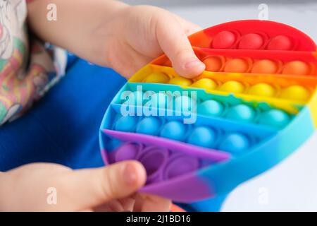 A child plays with pop it, children's hands close-up press on the pimples of anti-stress toys. Stock Photo