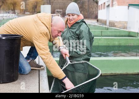 Male farmer with female worker catching sturgeons on farm Stock Photo
