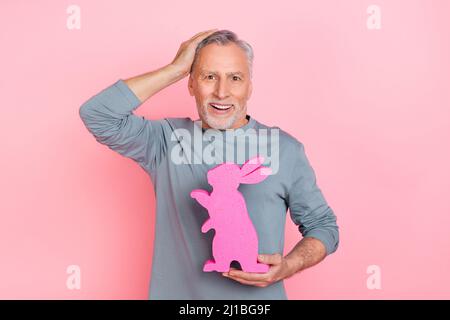 Photo of funny impressed man pensioner dressed grey shirt holding rabbit arm head isolated pink color background Stock Photo